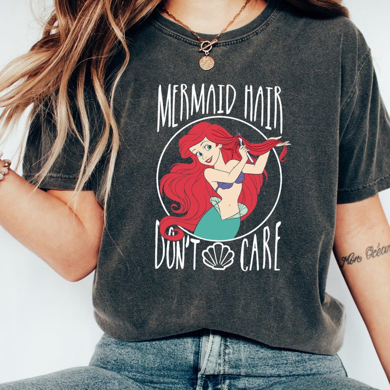 May include: A dark gray t-shirt with a graphic of Ariel from The Little Mermaid. The graphic shows Ariel brushing her hair and the text "Mermaid Hair Don't Care" with a seashell.