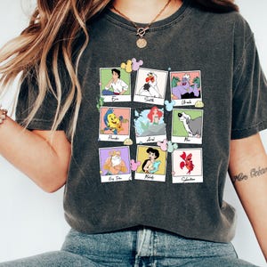May include: Dark grey t-shirt with a collage of cartoon characters in polaroid-style frames. Characters include Eric, Scuttle, Ursula, Flounder, Ariel, Max, King Triton, Melody, and Sebastian. Each frame is surrounded by a Mickey Mouse head.
