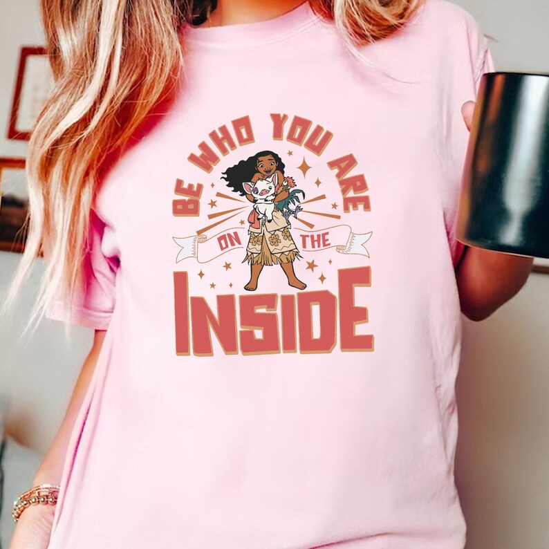 May include: Pink t-shirt with a graphic of a cartoon character holding a small animal. The graphic includes the text "Be who you are on the inside".