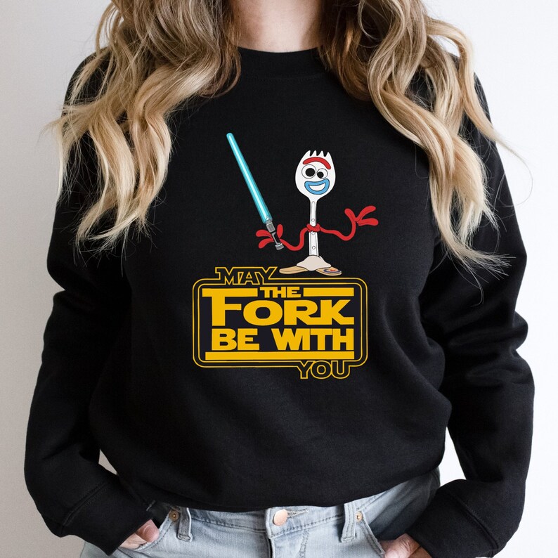 K&ouml;nnte beinhalten: Schwarzes Sweatshirt mit einem Grafikdruck einer Cartoon-Gabel, die ein Lichtschwert h&auml;lt. Der Text "M&ouml;ge die Gabel mit dir sein" ist in Gelb auf dem Sweatshirt gedruckt.