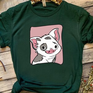 May include: A green t-shirt with a pink square featuring a cartoon pig with black and white spots. The pig has a pink nose and is smiling.