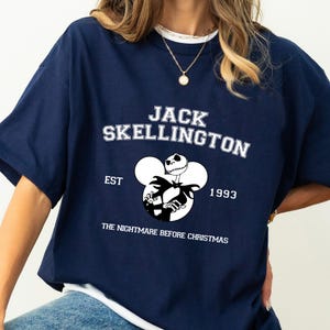 May include: A navy blue t-shirt with a white graphic of Jack Skellington from The Nightmare Before Christmas. The text "Jack Skellington" is printed in white above the graphic, and "EST 1993" is printed below the graphic.
