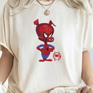 Puede incluir: Una camiseta blanca con una imagen de dibujos animados de un cerdo con un traje de Spiderman rojo y azul. El cerdo est&aacute; de pie con los brazos cruzados y un s&iacute;mbolo de ara&ntilde;a rojo y azul debajo.