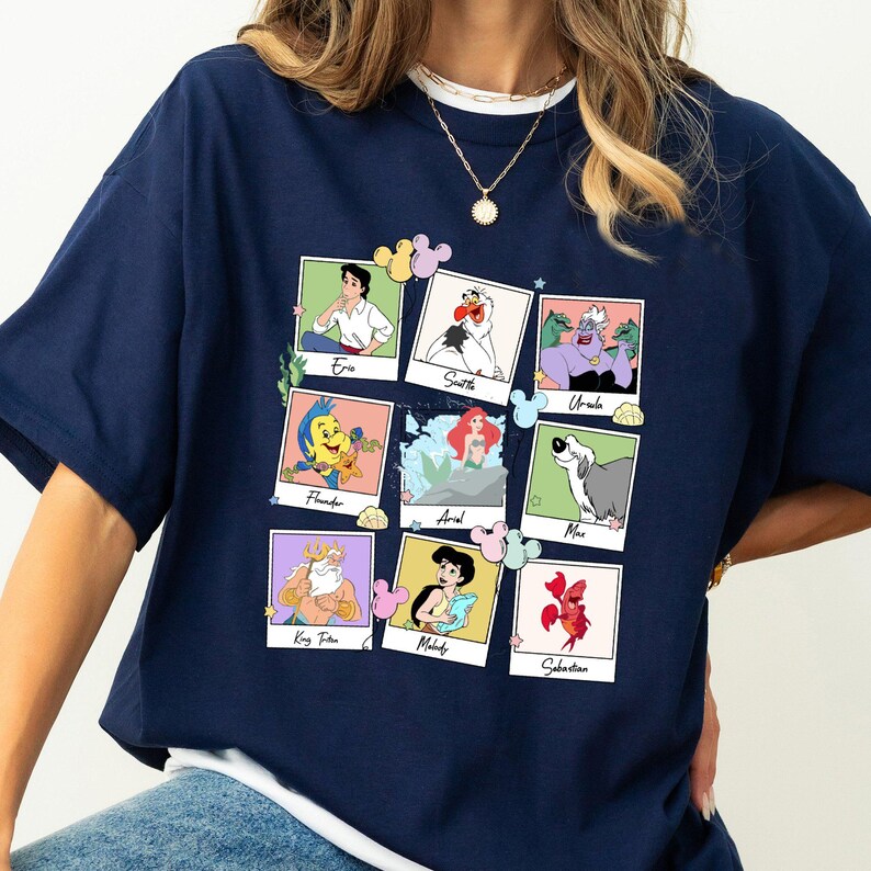 May include: A navy blue t-shirt displaying a collage of characters from a popular animated film. The collage includes images of Eric, Scuttle, Ursula, Flounder, Ariel, Max, King Triton, Melody, and Sebastian. The images are in a polaroid style.