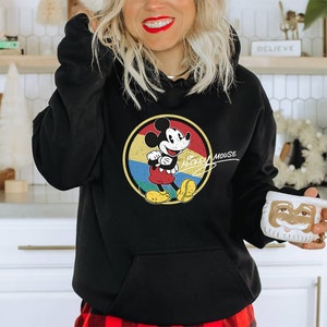 Puede incluir: Sudadera con capucha negra con un gr&aacute;fico de estilo vintage de Mickey Mouse en un c&iacute;rculo de colores. El texto "Mickey Mouse" est&aacute; escrito en cursiva blanca debajo del c&iacute;rculo.