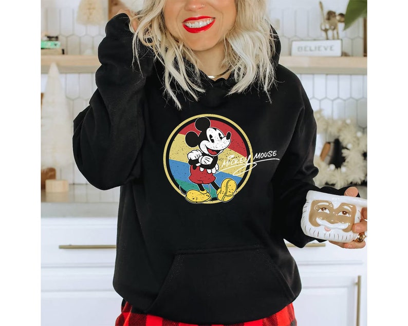 Puede incluir: Sudadera con capucha negra con un gr&aacute;fico de estilo vintage de Mickey Mouse en un c&iacute;rculo de colores. El texto "Mickey Mouse" est&aacute; escrito en cursiva blanca debajo del c&iacute;rculo.