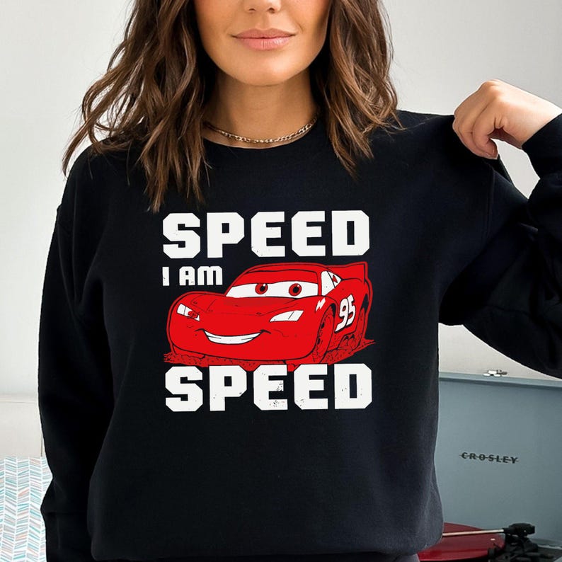Puede incluir: Sudadera negra con un coche de carreras rojo de dibujos animados y el texto "Speed I am Speed" en blanco.