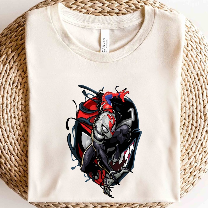 Puede incluir: Una camiseta blanca con un gr&aacute;fico de Venom y Spider-Man. Venom est&aacute; en primer plano, con Spider-Man detr&aacute;s de &eacute;l. Venom es negro con ojos y dientes blancos, y Spider-Man es rojo y azul.