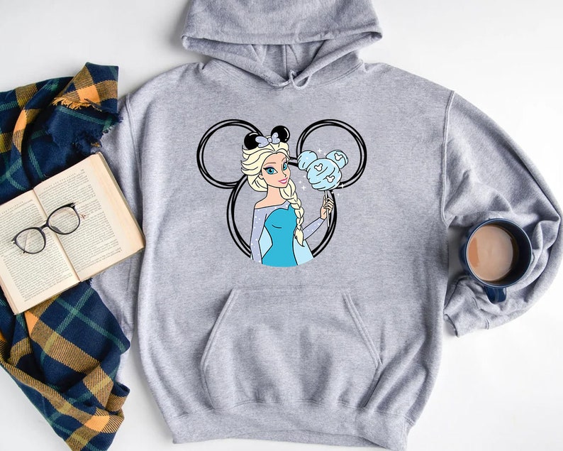 Puede incluir: Sudadera gris con capucha con una ilustraci&oacute;n en blanco y negro de una princesa Disney con cabello azul sosteniendo un dulce con forma de Mickey Mouse azul.