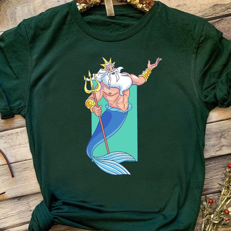 K&ouml;nnte beinhalten: Ein gr&uuml;nes T-Shirt mit einem Cartoon-Bild von K&ouml;nig Triton aus Disneys Arielle, die Meerjungfrau. Er h&auml;lt einen Dreizack und hat einen blauen Schwanz.