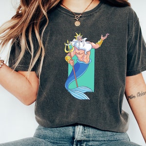 K&ouml;nnte beinhalten: Ein dunkelgraues T-Shirt mit einem Cartoon-Bild von K&ouml;nig Triton aus Arielle, die Meerjungfrau. Er h&auml;lt seinen Dreizack und hat einen blauen Schwanz.