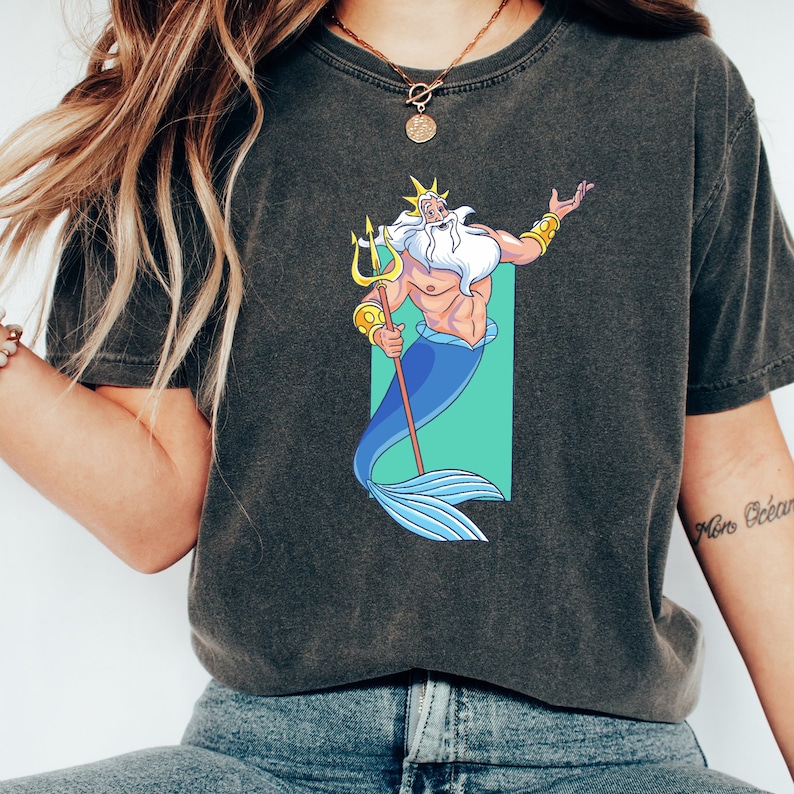K&ouml;nnte beinhalten: Ein dunkelgraues T-Shirt mit einem Cartoon-Bild von K&ouml;nig Triton aus Arielle, die Meerjungfrau. Er h&auml;lt seinen Dreizack und hat einen blauen Schwanz.