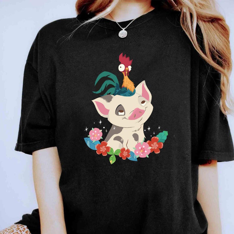 K&ouml;nnte beinhalten: Schwarzes T-Shirt mit einem Cartoon-Bild eines Schweins mit einem Hahn auf dem Kopf. Das Schwein und der Hahn sind von Blumen umgeben.