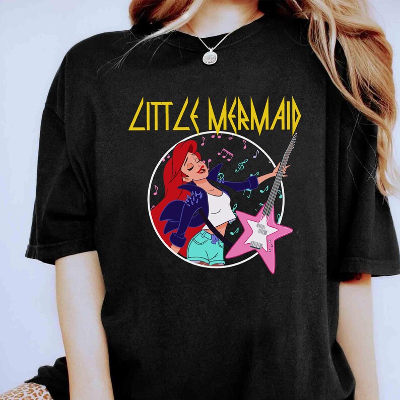 May include: Black t-shirt with a graphic of Ariel from The Little Mermaid playing an electric guitar. The text "Little Mermaid" is above the graphic.