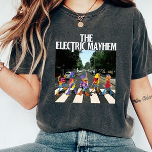 May include: A dark gray t-shirt with a graphic of five cartoon figures walking across a crosswalk. The text "THE ELECTRIC MAYHEM" is printed above the graphic.
