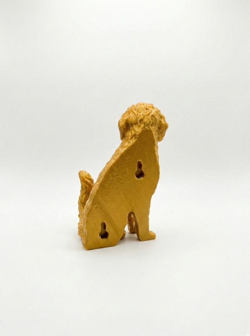 May include: A golden-colored dog-shaped wall hook, viewed from the back, with a textured, curly coat and tail. The dog is sitting, with three keyhole-shaped openings on its back for mounting. The background is plain white.