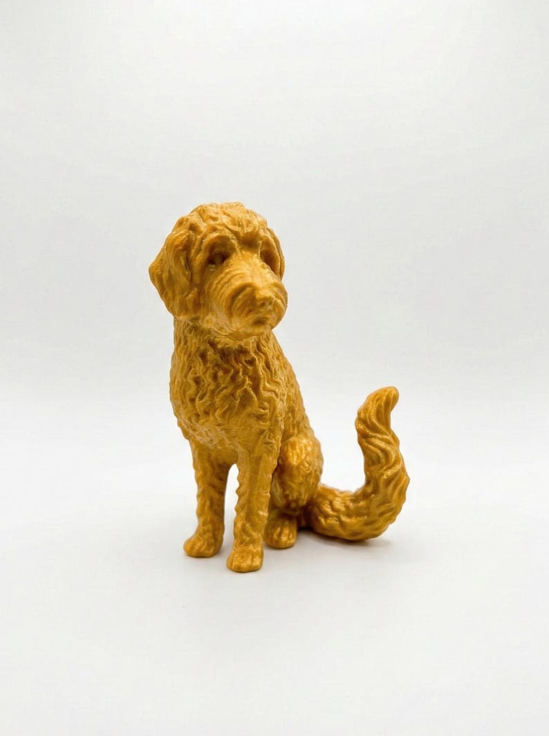 May include: A golden-colored figurine of a dog in a sitting position with a curly tail. The dog has a textured coat and is set against a white background. The figurine is a decorative item.