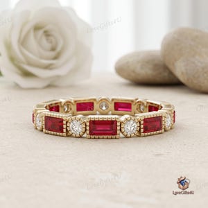 May include: A gold eternity band featuring alternating baguette-cut red rubies and round brilliant-cut white diamonds. The stones are set in a milgrain-edged metal frame, creating a continuous pattern of rectangular and circular shapes around the ring.