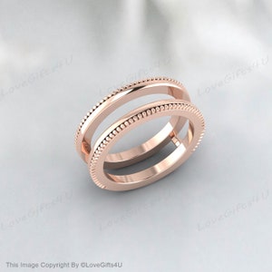 Puede incluir: Dos anillos de oro rosa con un diseño de cuentas en los bordes. Los anillos están apilados, uno ligeramente por encima del otro. El fondo es de un color suave y neutro.