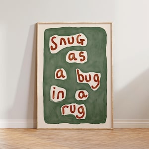Peut inclure: Impression d'art encadrée avec l'expression "Snug as a bug in a rug" en lettres marron sur fond vert. L'œuvre est dans un cadre en bois clair, pour la décoration intérieure.