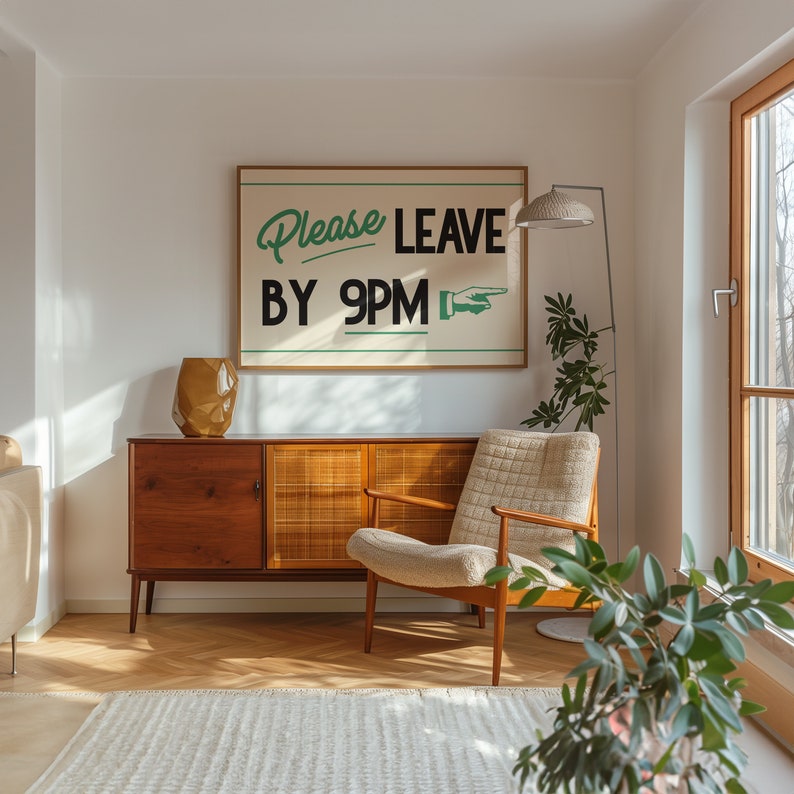 May include: A mid-century modern living room scene featuring a wooden cabinet, a beige armchair, and a large framed sign that reads "Please LEAVE BY 9PM." A gold-colored vase and a floor lamp with a woven shade are also visible.