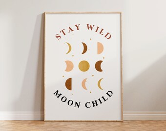 May include: A framed print with the text "Stay Wild Moon Child" in brown and black lettering. The print features a design of various moon phases in shades of peach, brown, and gold.