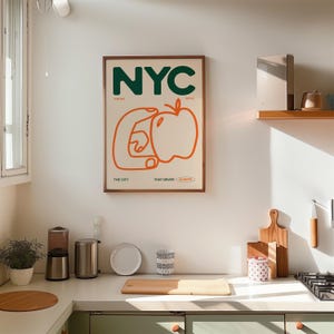 May include: A framed print with the text "NYC" in green letters, with the words "The Big Apple" and "The City That Never Sleeps" below. The print features a stylized orange hand holding a red apple.