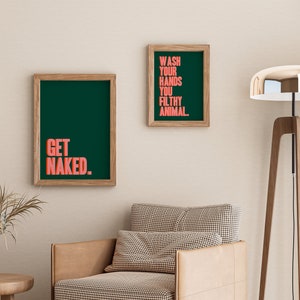 May include: Two rectangular wall art prints in light wood frames. The larger print features the text GET NAKED in coral pink on a dark green background. The smaller print features the text WASH YOUR HANDS YOU FILTHY ANIMAL in coral pink on dark green.