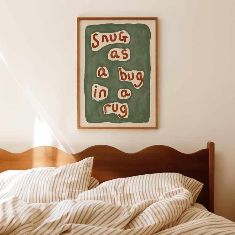 May include: A framed art print with the words "snug as a bug in a rug" in a playful font. The artwork features a green background with the text in a mix of white and red. The print is displayed above a bed with striped bedding.