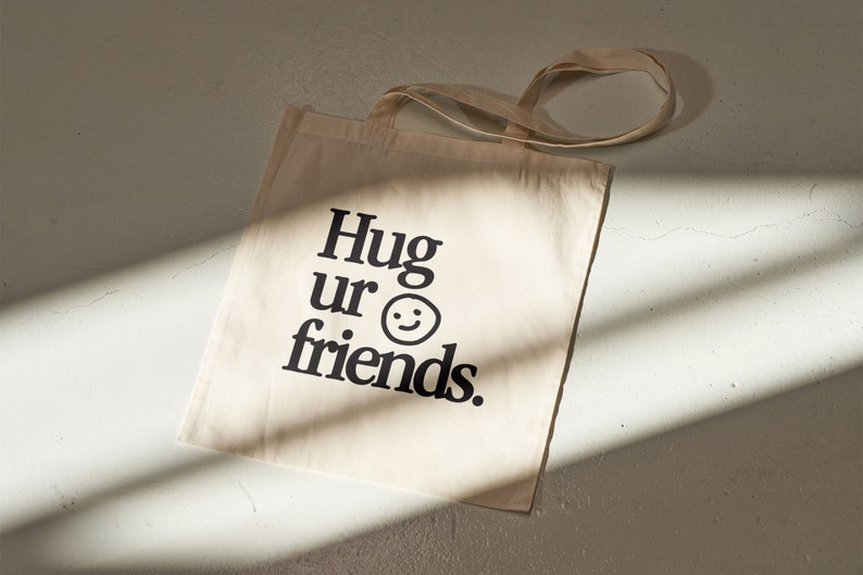 May include: A beige canvas tote bag with black text that reads "Hug ur friends." and a simple smiley face.