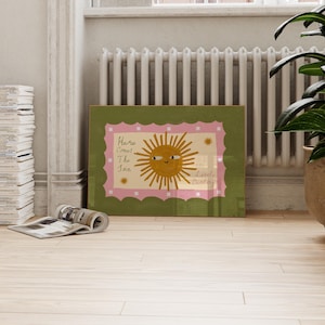 Puede incluir: Una impresi&oacute;n art&iacute;stica enmarcada con una ilustraci&oacute;n de un sol sonriente y el texto "Here Comes The Sun, Little Darling". La obra de arte tiene un borde verde, un borde interior rosa festoneado y un fondo crema.