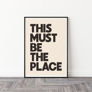 Puede incluir: Impresi&oacute;n tipogr&aacute;fica en blanco y negro con el texto "THIS MUST BE THE PLACE" sobre un fondo crema. La impresi&oacute;n est&aacute; enmarcada en un marco negro.