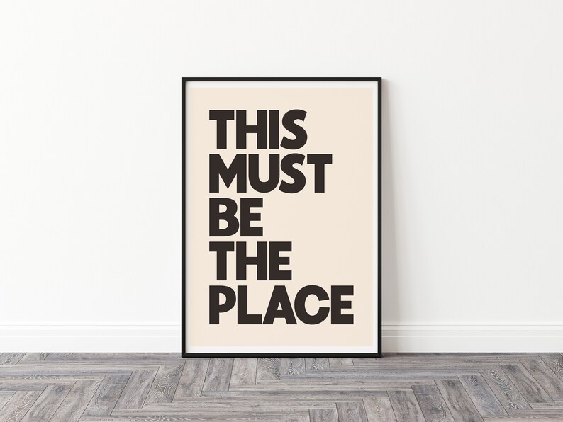 Puede incluir: Impresi&oacute;n tipogr&aacute;fica en blanco y negro con el texto "THIS MUST BE THE PLACE" sobre un fondo crema. La impresi&oacute;n est&aacute; enmarcada en un marco negro.