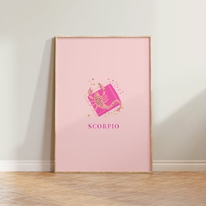 May include: A framed vertical wall art print featuring a light pink background with a central illustration of a scorpion on a bright pink square. The design includes small gold stars and dots, with the word SCORPIO printed in pink capital letters.
