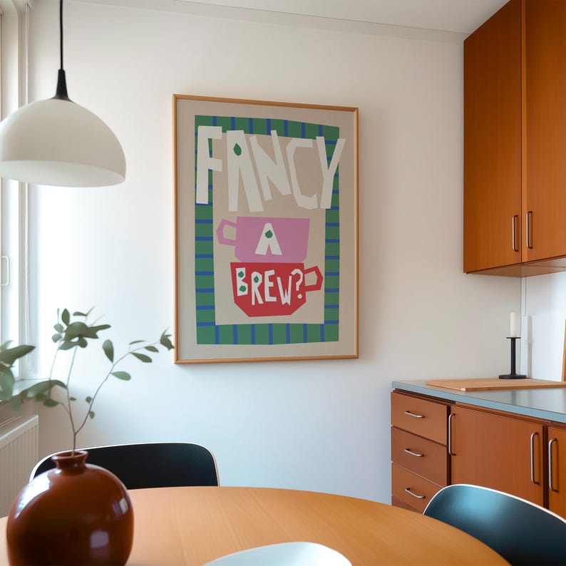 Op de afbeelding: Een ingelijste poster met de tekst "Fancy a Brew?" in een kleurrijke, abstracte stijl. De poster toont een gestileerde afbeelding van een theekopje en een mok.