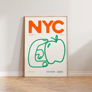 May include: A white poster with the word "NYC" in orange letters. The poster has a green illustration of a hand holding an apple with the text "The Big Apple" below the word "NYC". Below the illustration, the text reads "The City That Never Sleeps".