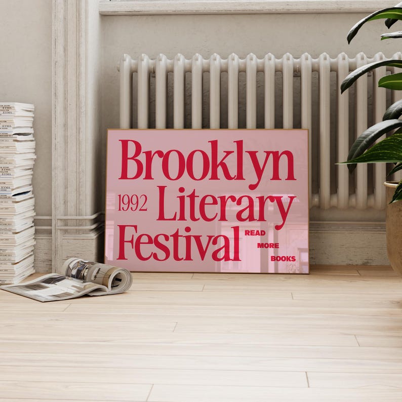 May include: A pink poster with the words "Brooklyn 1992 Literary Festival" in red. The poster also includes the words "Read More Books". The poster is leaning against a white radiator.