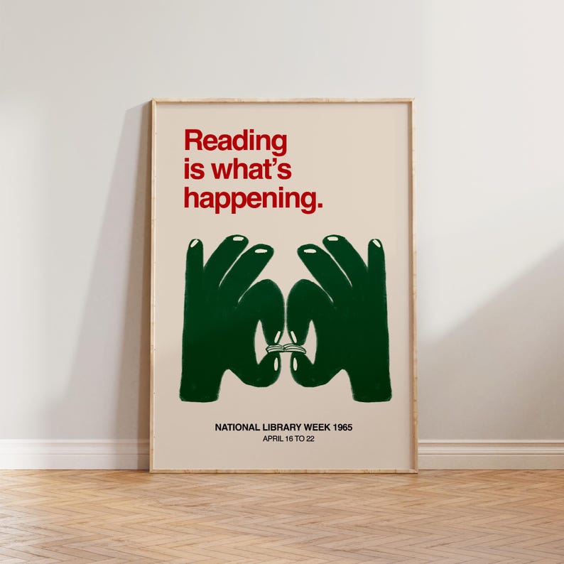 May include: A framed poster with the text "Reading is what's happening" in red. Below, two green hands form a circle around a book. The poster is for National Library Week 1965, April 16 to 22.