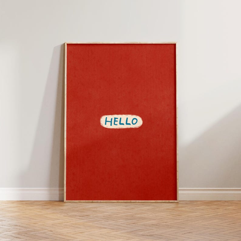 Puede incluir: Una impresi&oacute;n art&iacute;stica enmarcada con un fondo rojo liso. La palabra "HELLO" est&aacute; escrita en blanco con un contorno azul en forma de rect&aacute;ngulo redondeado. El marco es de color madera clara.