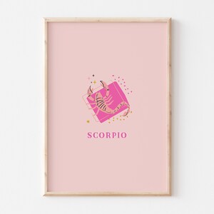 May include: A framed wall art print featuring a light pink background with a central graphic of a pink scorpion positioned over a darker pink square. The word SCORPIO is printed in pink capital letters below the graphic, accented by small stars and dots.