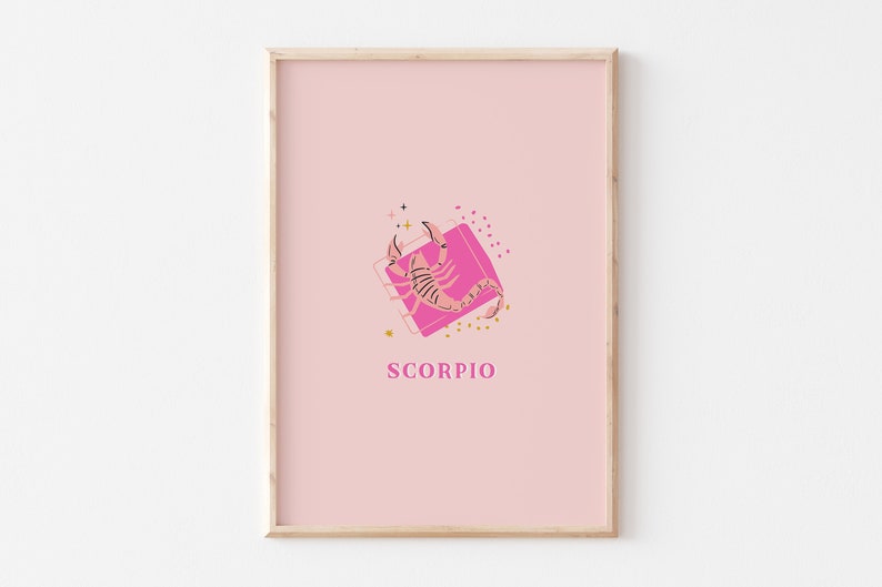 May include: A framed wall art print featuring a light pink background with a central graphic of a pink scorpion positioned over a darker pink square. The word SCORPIO is printed in pink capital letters below the graphic, accented by small stars and dots.