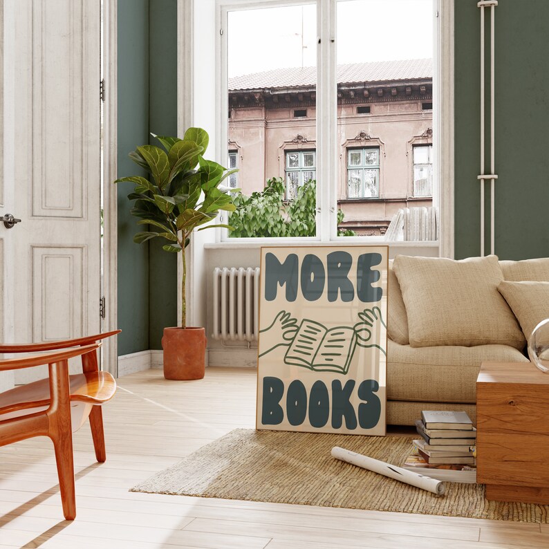 Peut inclure: Une affiche avec le texte "MORE BOOKS" dans une police de caract&egrave;res audacieuse et stylis&eacute;e. L'affiche repr&eacute;sente une main qui tend la main pour saisir un livre, qui est ouvert et dont les pages sont visibles. L'affiche est sur un mur brun clair, avec une plante verte dans un pot brun au premier plan.