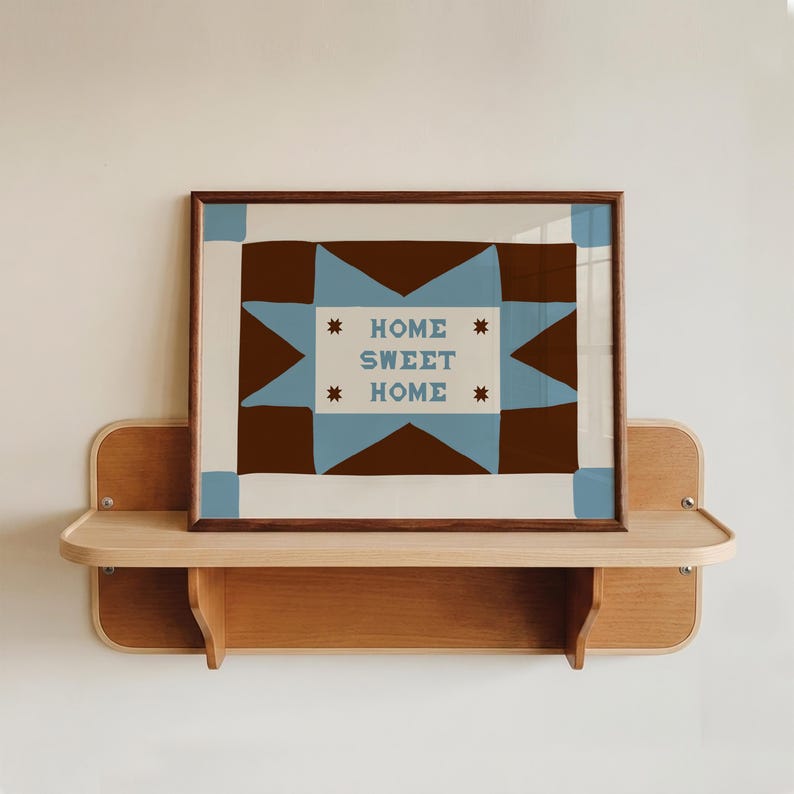 Puede incluir: Una l&aacute;mina de arte mural rectangular en un marco de madera oscura con un patr&oacute;n geom&eacute;trico de estrellas en marr&oacute;n y azul claro sobre un fondo crema. El centro del dise&ntilde;o muestra el texto HOME SWEET HOME en letras azules con estrellas marrones.