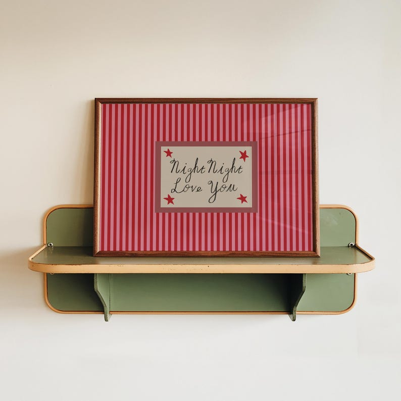 K&ouml;nnte beinhalten: Ein gerahmter Druck mit einem rot-rosa gestreiften Hintergrund und dem Text "Night Night Love You". Der Druck wird auf einem gr&uuml;nen und holzfarbenen Regal pr&auml;sentiert, was eine charmante, Vintage-&Auml;sthetik erzeugt.