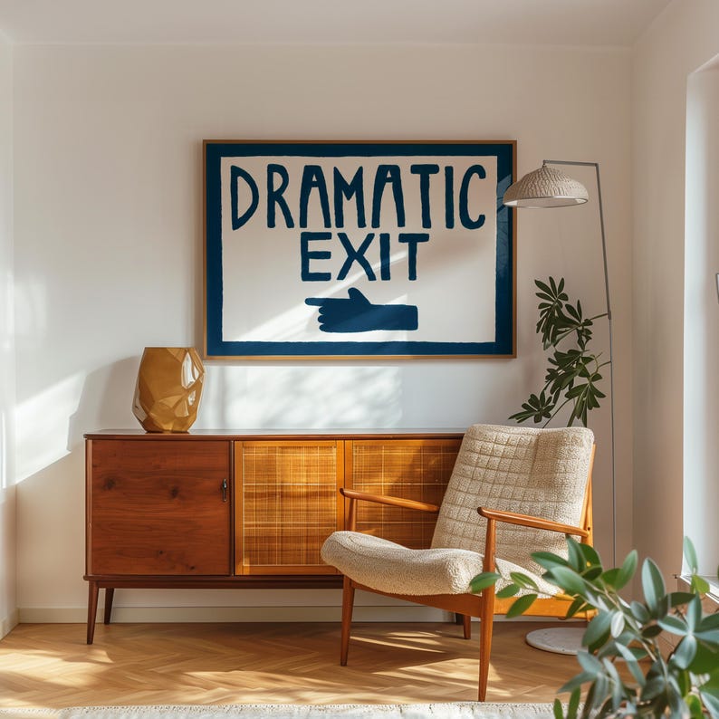 Puede incluir: Una impresi&oacute;n enmarcada en blanco con el texto "DRAMATIC EXIT" en letras azules y una mano azul apuntando hacia la derecha. La impresi&oacute;n est&aacute; colgada en una pared blanca sobre un armario de madera de estilo moderno de mediados de siglo con una puerta de rat&aacute;n tejido. Un sill&oacute;n beige con respaldo y asiento de tejido tejido se encuentra frente al armario. Una planta en maceta se encuentra en el suelo junto a la silla.