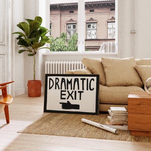 Puede incluir: Un cartel en blanco y negro con el texto "Dramatic Exit" y una mano negra apuntando hacia la derecha. El cartel est&aacute; apoyado en un sof&aacute; beige en una sala de estar.