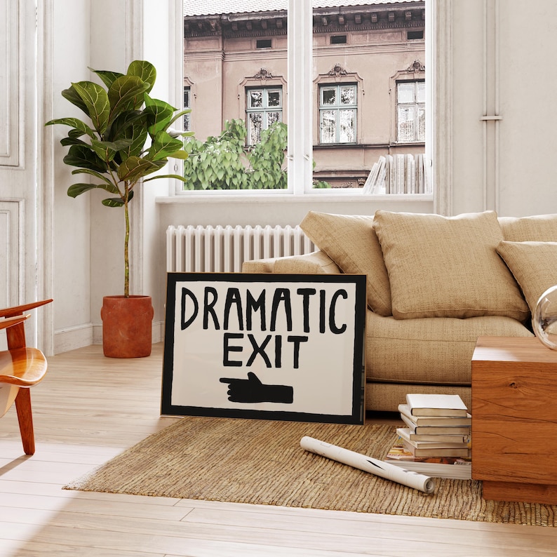 Puede incluir: Un cartel en blanco y negro con el texto "Dramatic Exit" y una mano negra apuntando hacia la derecha. El cartel est&aacute; apoyado en un sof&aacute; beige en una sala de estar.