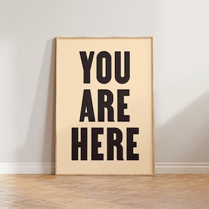 Peut inclure: Une affiche encadr&eacute;e avec le texte "YOU ARE HERE" en lettres noires et grasses sur un fond beige clair.