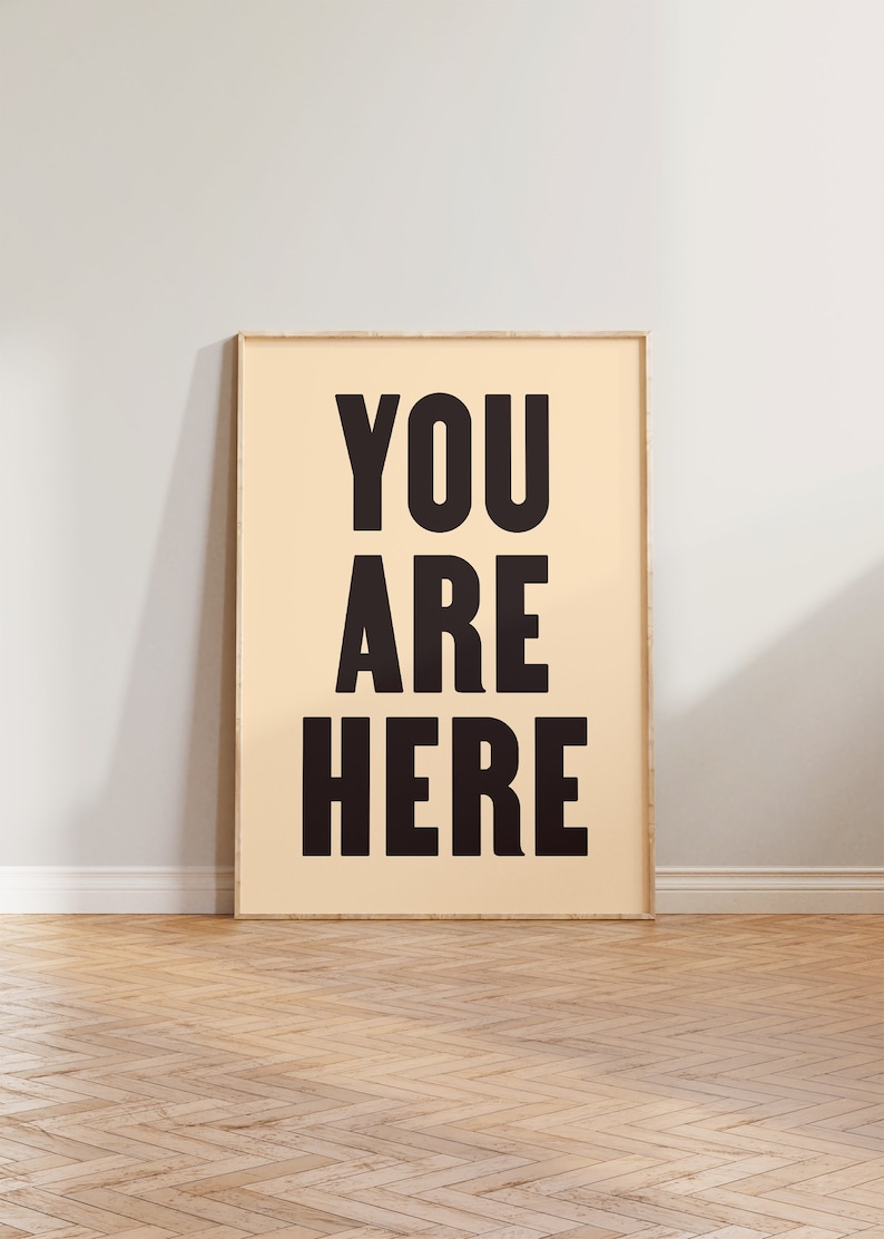 Peut inclure: Une affiche encadr&eacute;e avec le texte "YOU ARE HERE" en lettres noires et grasses sur un fond beige clair.