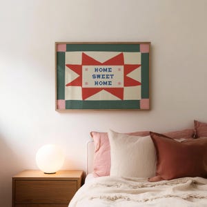 Puede incluir: Una l&aacute;mina decorativa rectangular en un marco de madera con un patr&oacute;n inspirado en una colcha, con una gran estrella roja sobre un fondo crema. El texto "HOME SWEET HOME" est&aacute; impreso en letras azules en el centro, flanqueado por peque&ntilde;as cruces rosas.